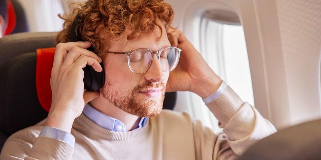 Smiling passenger with red hair wearing headphones by the window seat.