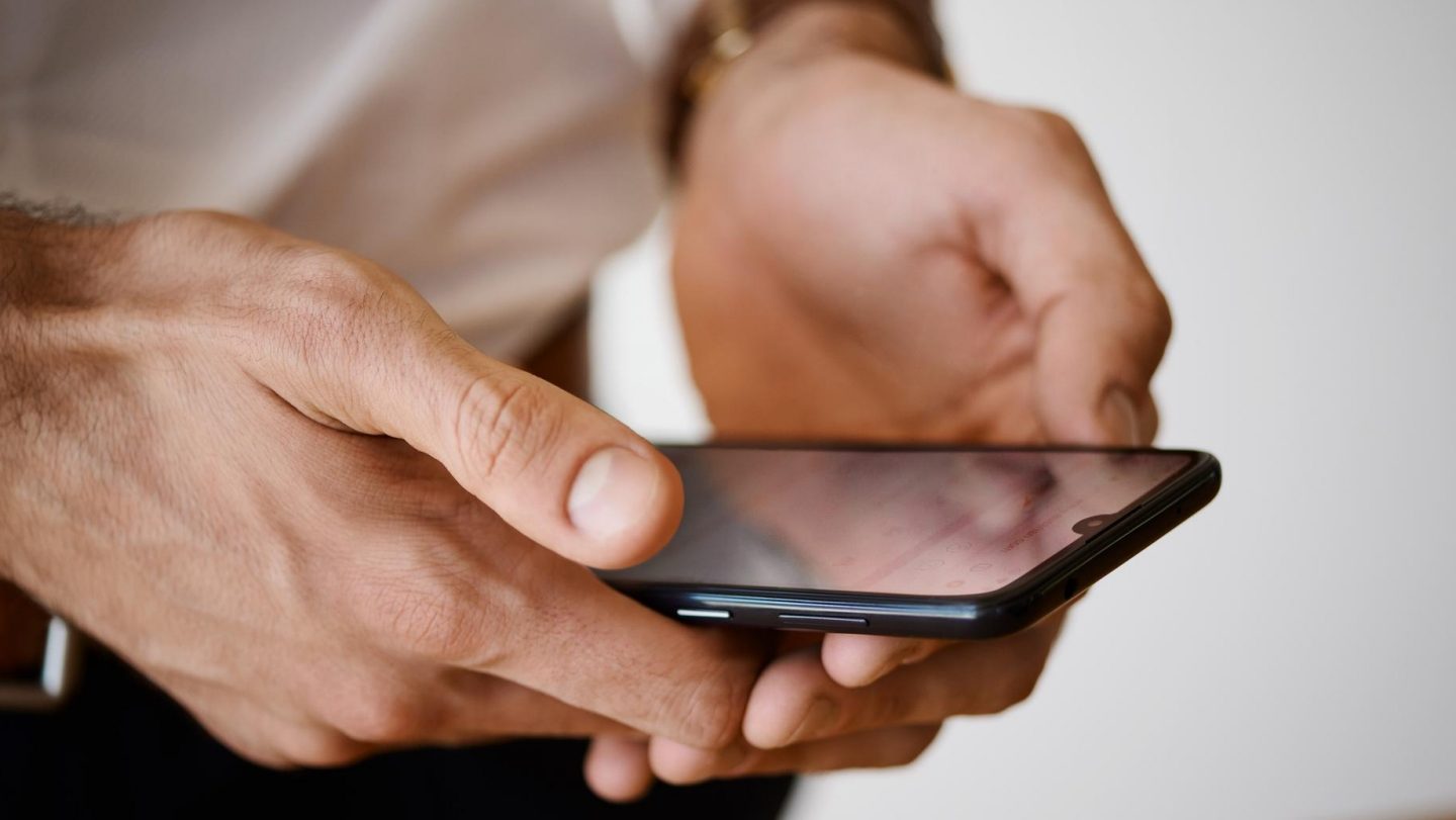 A close-up of a person's hands typing on a smartphone keyboard.