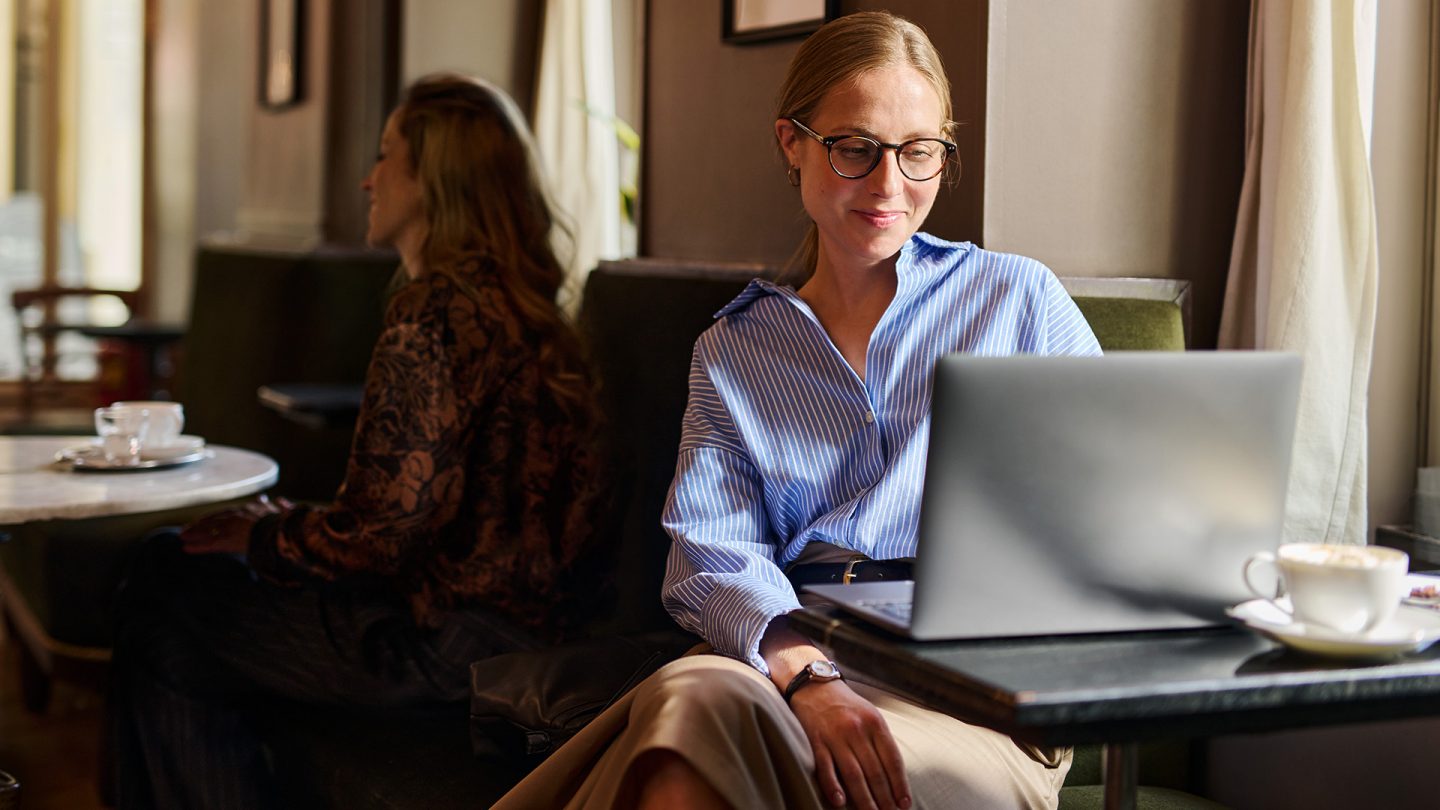 A woman with glasses sitting at a cafe table working on her laptop.