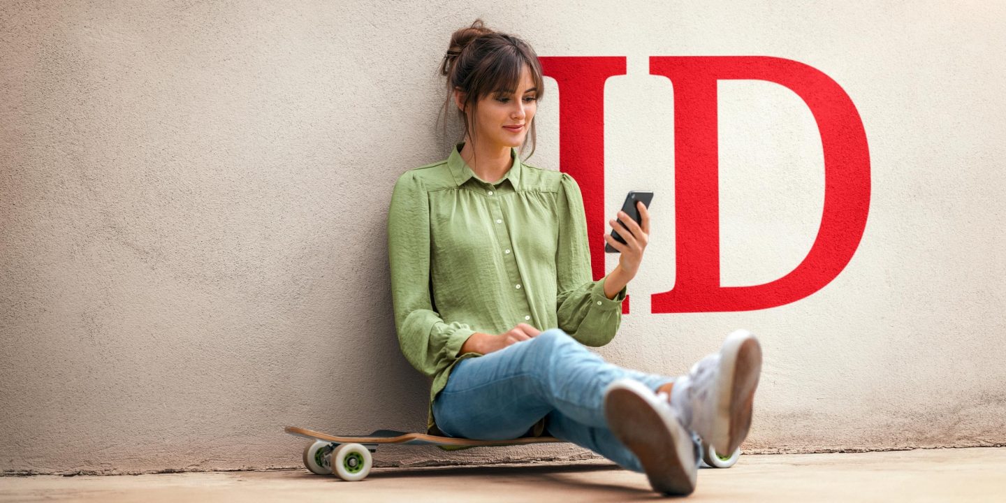 Young woman sitting on skateboard, using smartphone