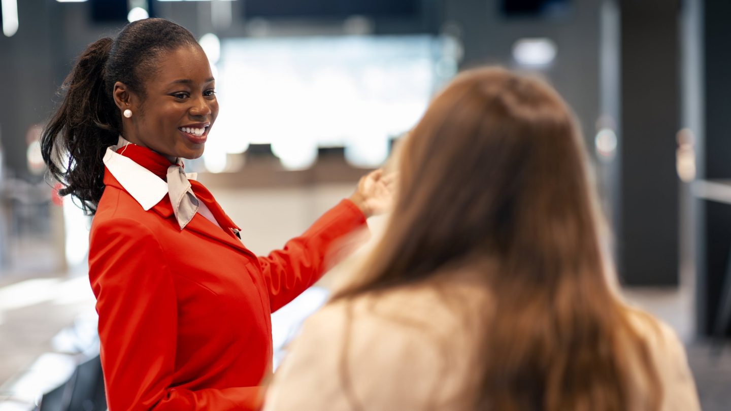 A smiling flight attendant in a red uniform looking at a passenger.