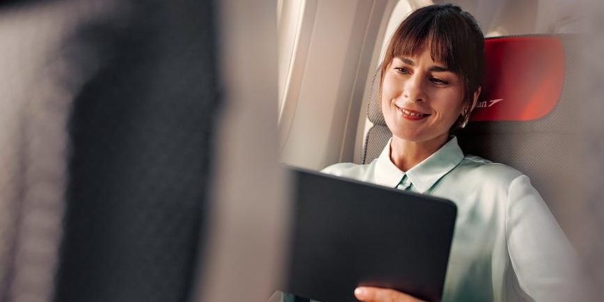 Woman using a tablet on an airplane with a red headrest.