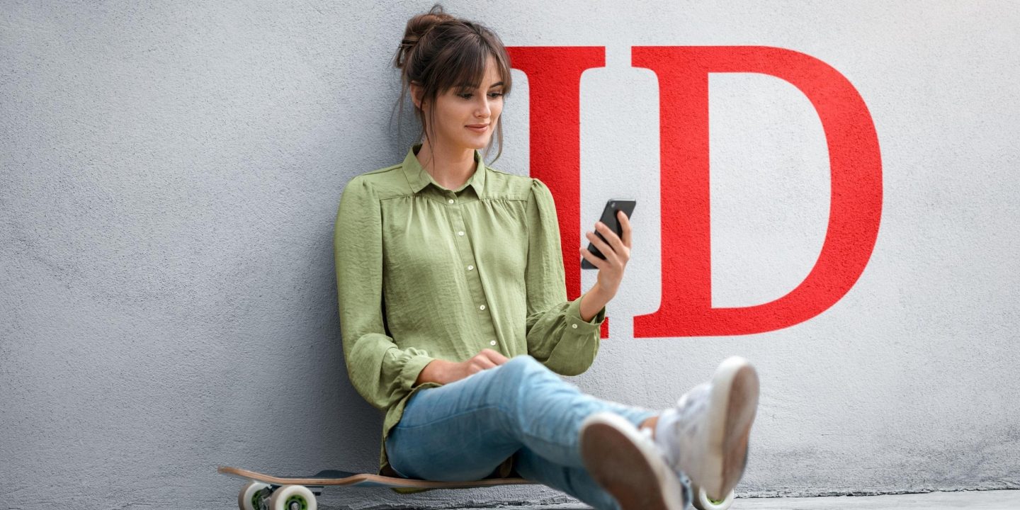A young woman sitting on a skateboard checking the conditions on her smartphone