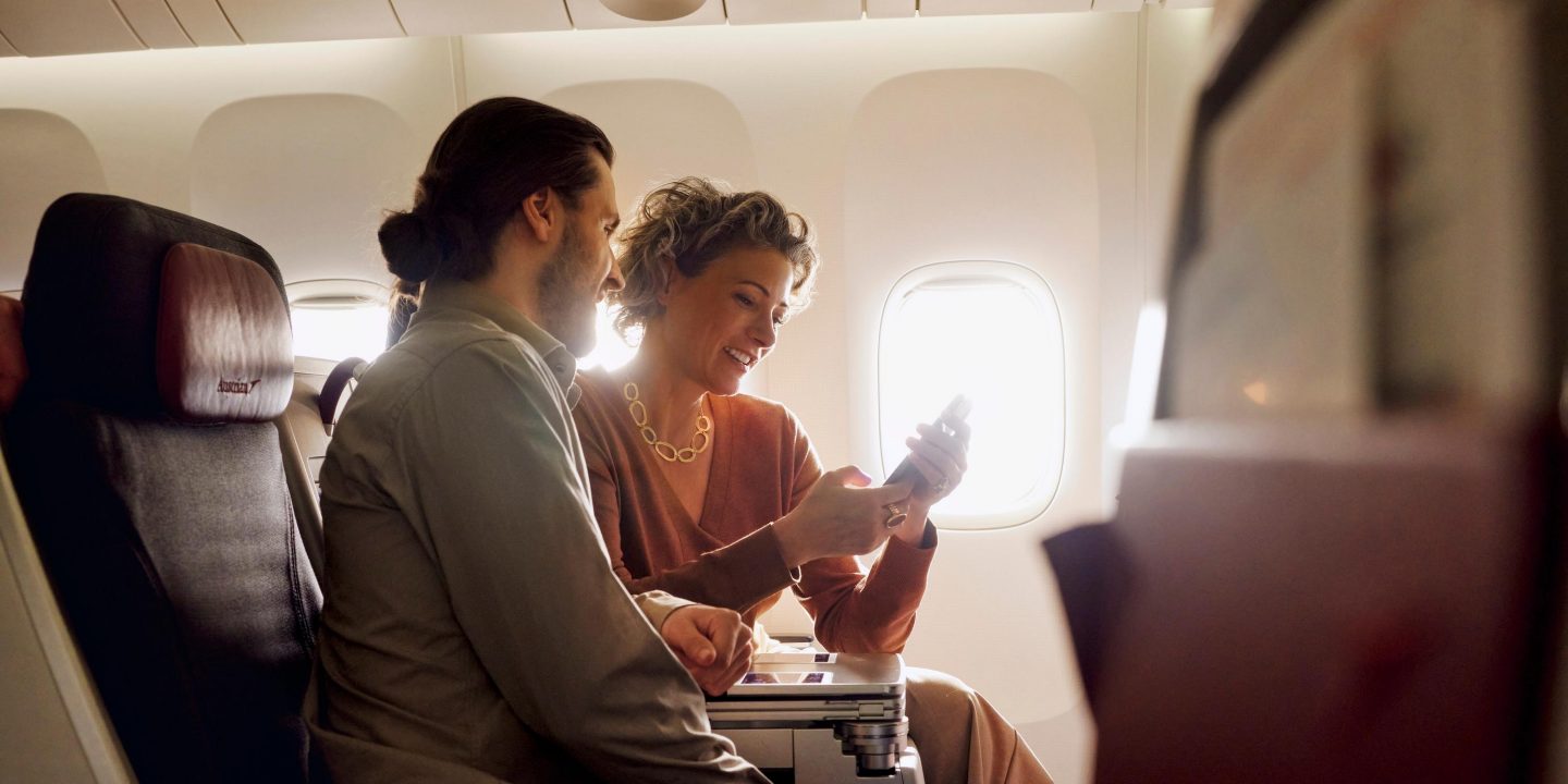 Couple sitting together in an airplane cabin, looking at a smartphone.