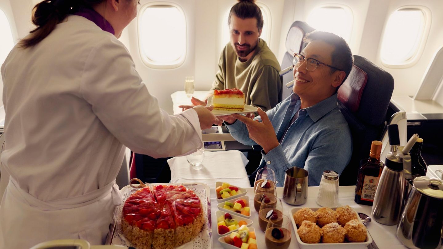 A man serves food to two passengers on an airplane.