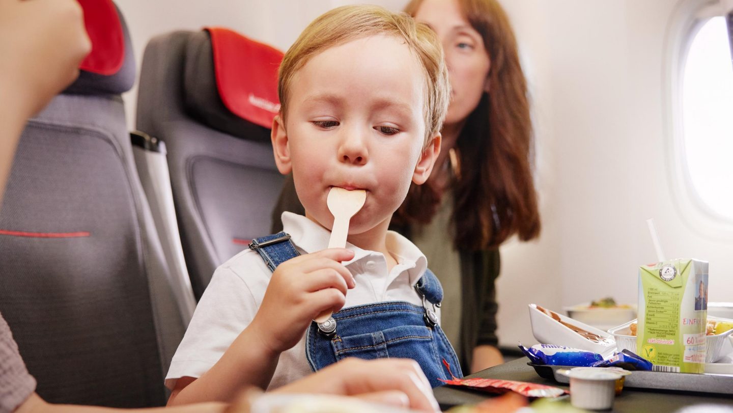 A young child takes a spoonful of food on an airplane.