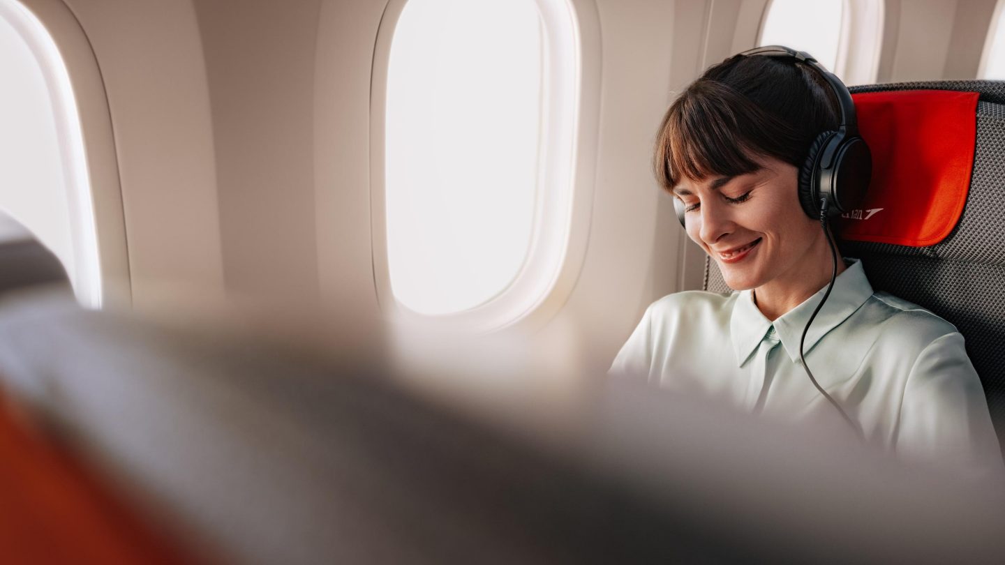 Passenger with noise-canceling headphones relaxing in a Premium Economy seat.