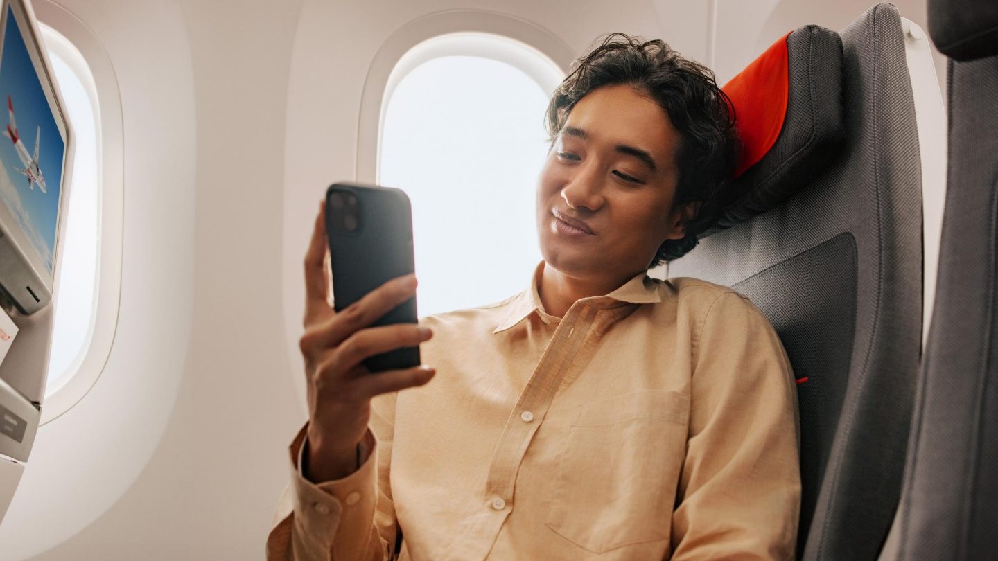 Passenger seated in an economy seat looking at their phone with a smile on their face.