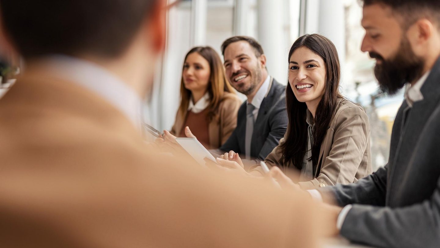 Smiling business team discussing work in meeting using laptop and documents in conference room. Successful business woman and businessmen discussing marketing strategy and ideas at meeting room. Corporate business man and woman with manager and secretary working together.