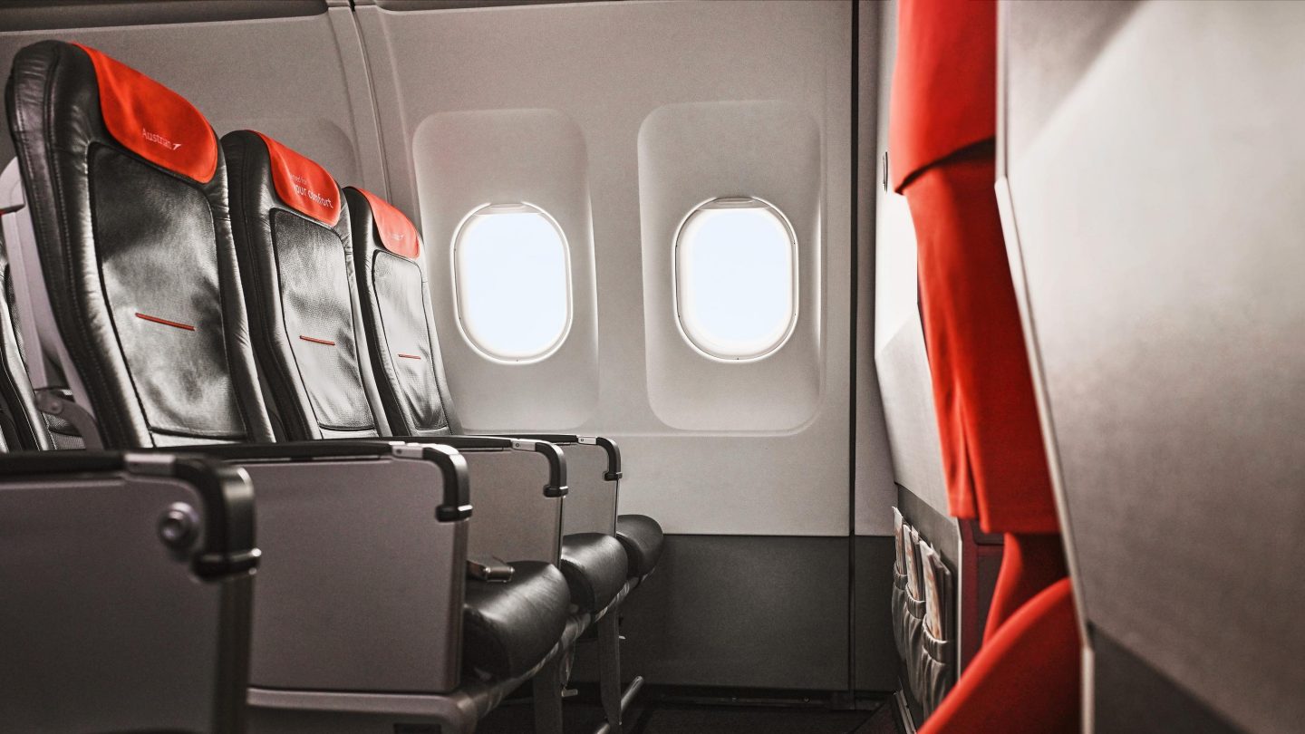 Austrian Airlines cabin: dark seats, orange headrests, and bright windows.