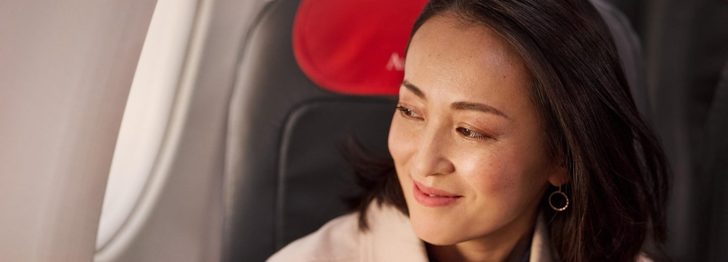 A passenger sits in an airplane seat, surrounded by soft lighting and the interior details of the aircraft.
