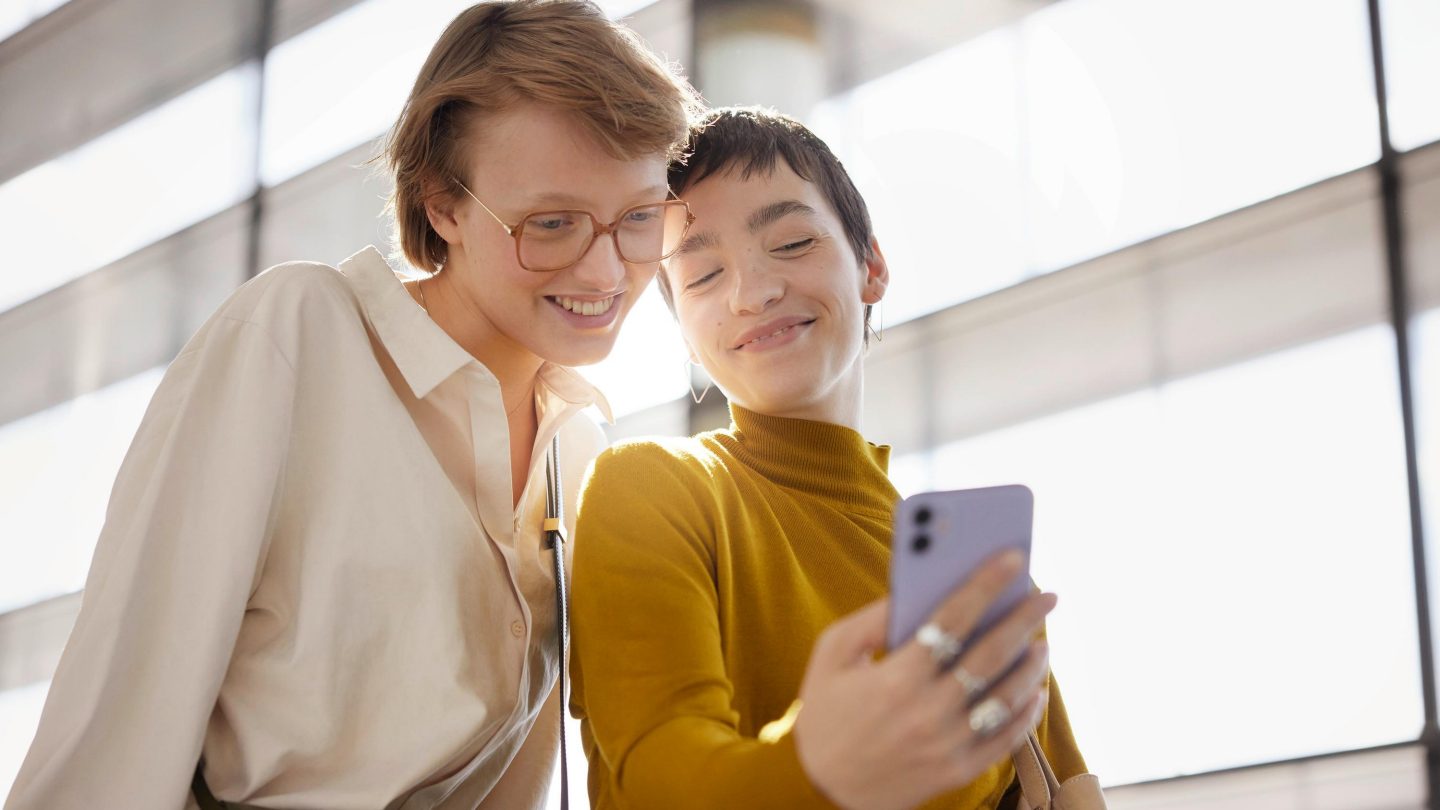 Two women smiling and looking together at a smartphone screen.