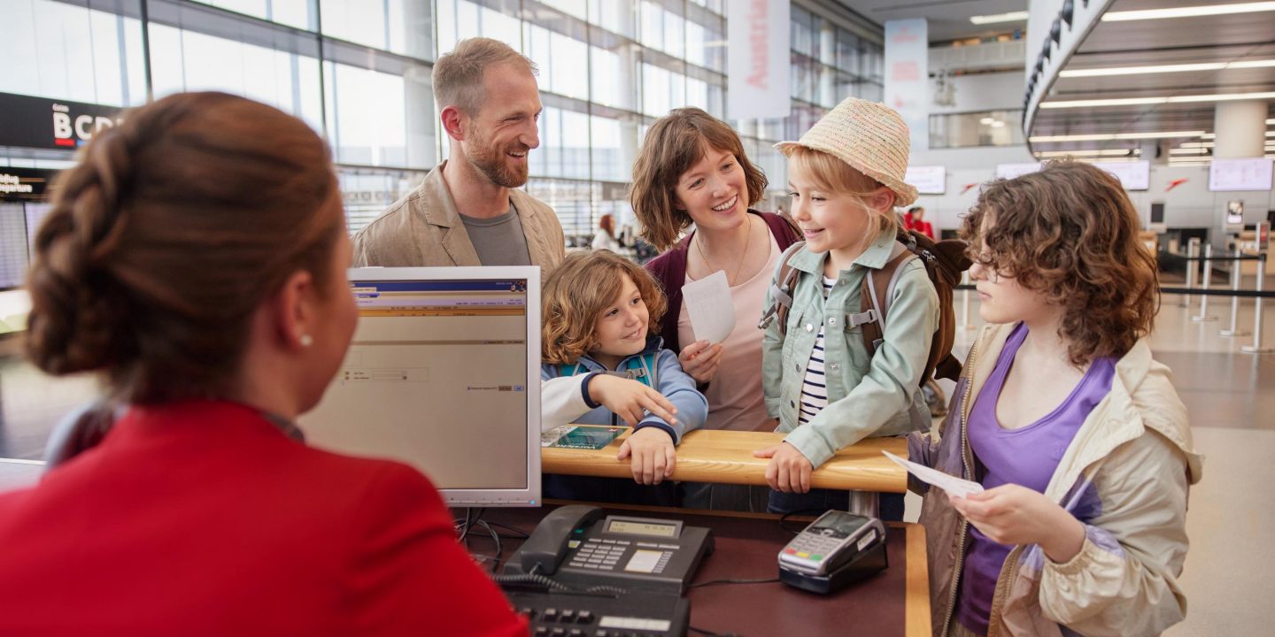 Eine glückliche Familie am Check-in-Schalter eines Flughafens, die von einem Mitarbeiter der Fluggesellschaft betreut wird.