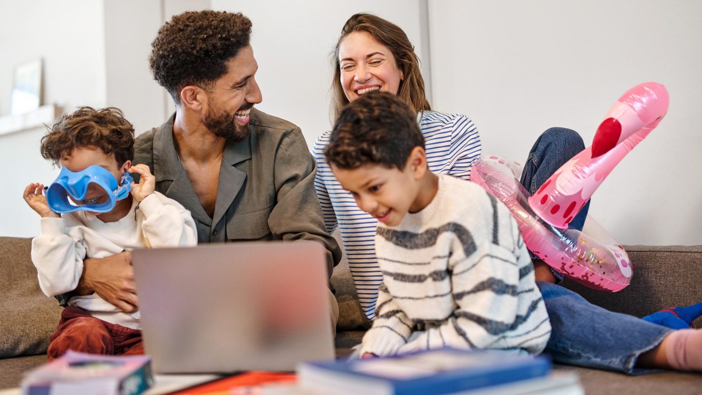 Smiling family sitting together on the floor looking at a laptop.