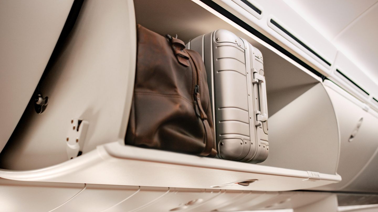 A suitcase rests on an airplane shelf, ready for travel.