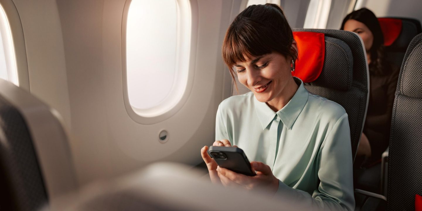 Passenger seated in a premium economy seat looking at their phone with a smile on their face. 