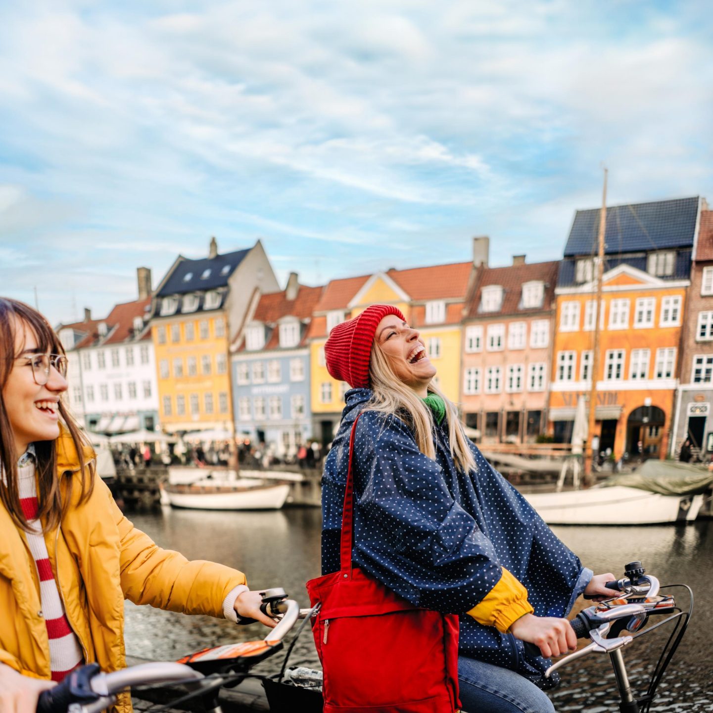 Two women laughing while cycling next to a waterfront canal.