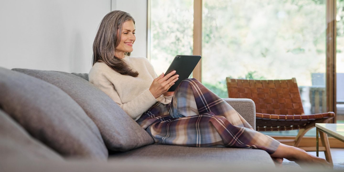 A woman on the sofa looking at her iPad and laughing