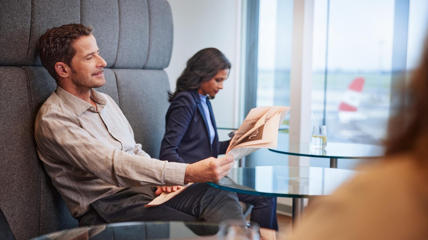 Business travelers reading newspapers in a modern airport lounge.