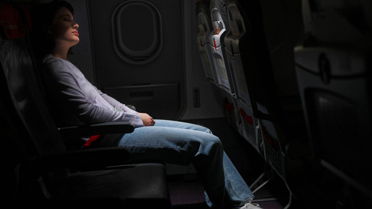 A person leans back in a dimly lit airplane seat, appearing calm and relaxed.