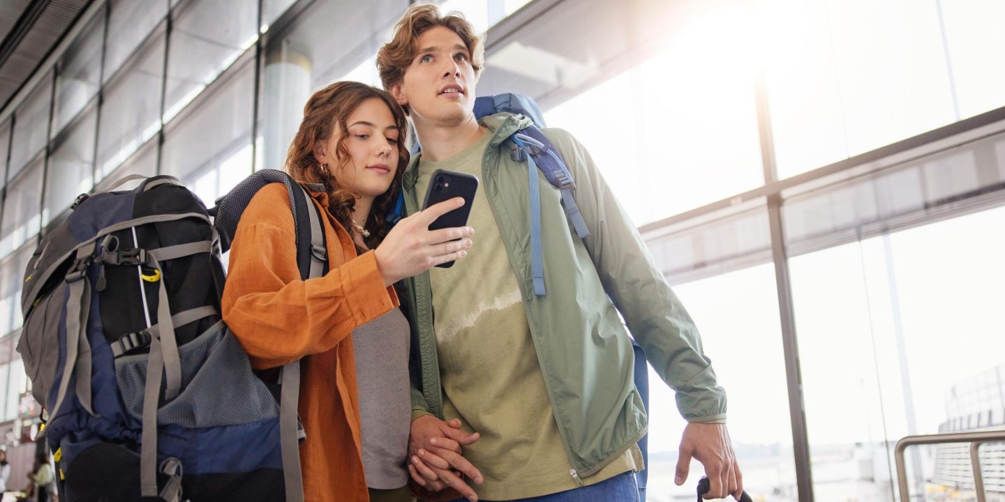A man and woman with backpacks are waiting in an airport.