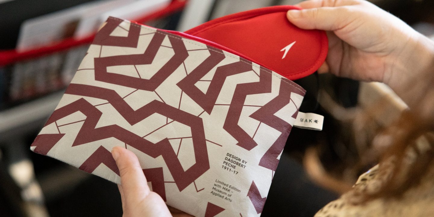 A woman displaying a red and white patterned bag, emphasizing luxury and style.