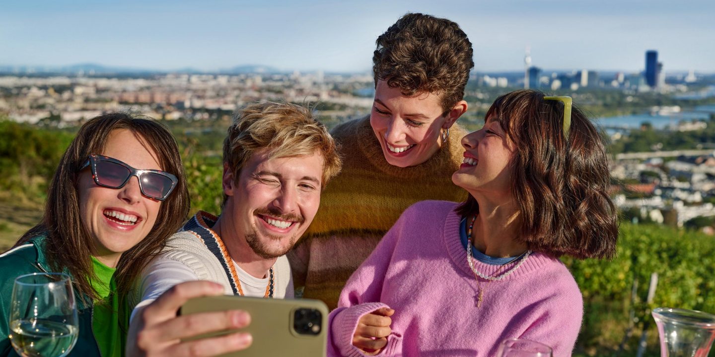Vier Freunde, die lächeln und draußen ein Selfie machen.
