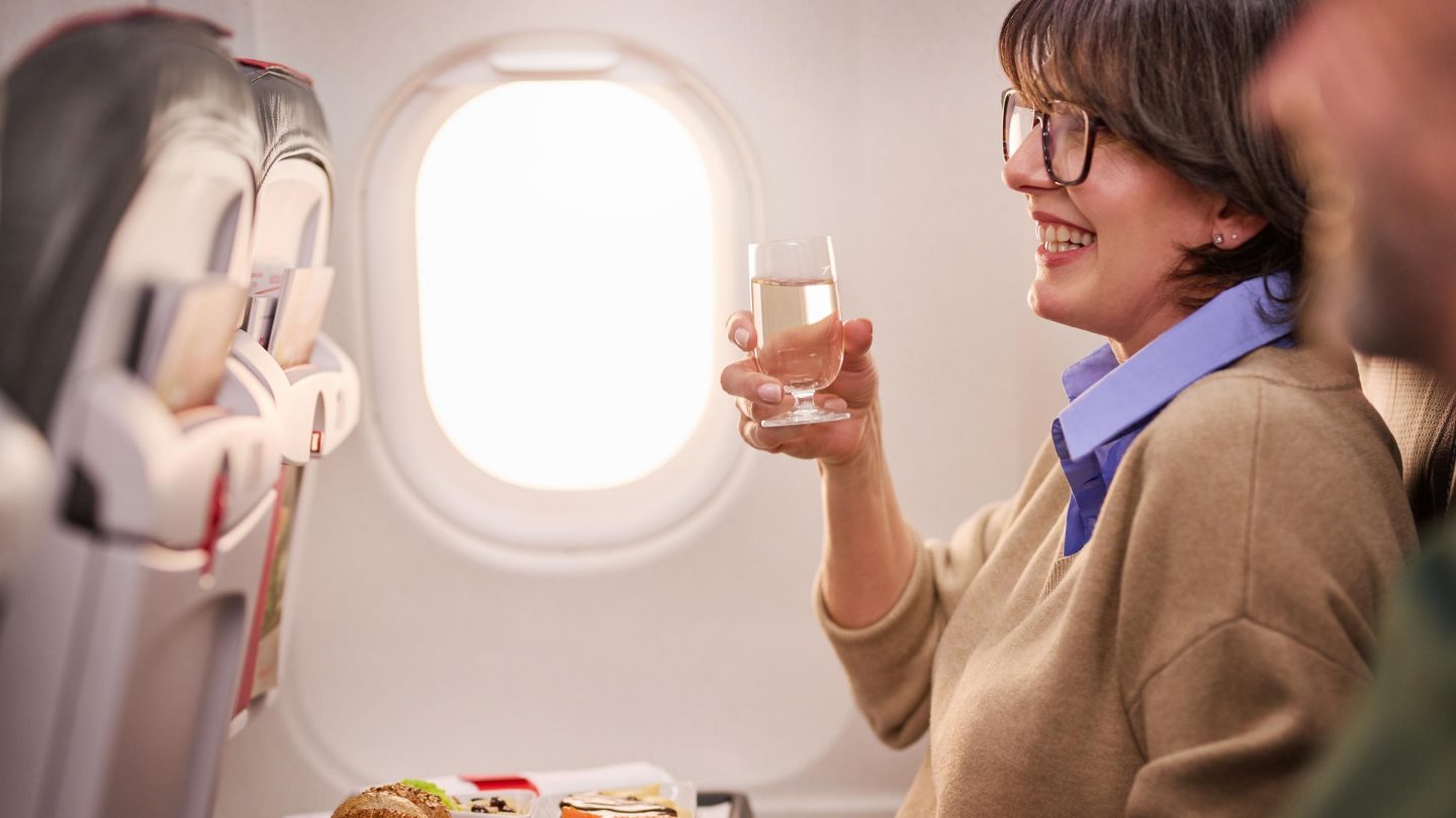 A woman drinks wine in a cozy airplane section, taking advantage of the comfort & an adjacent free seat.
