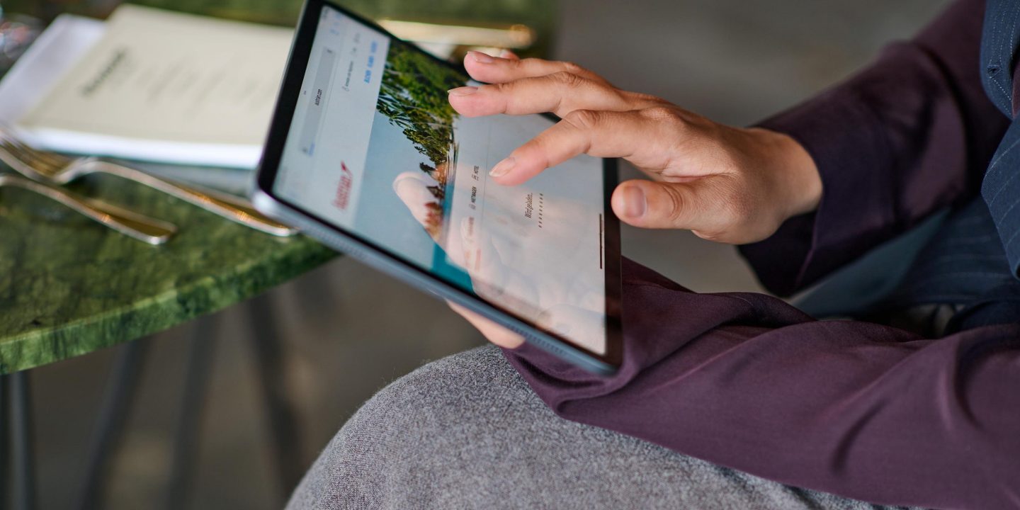 Hände, die mit einem Tablet auf einer Reise-Website surfen.