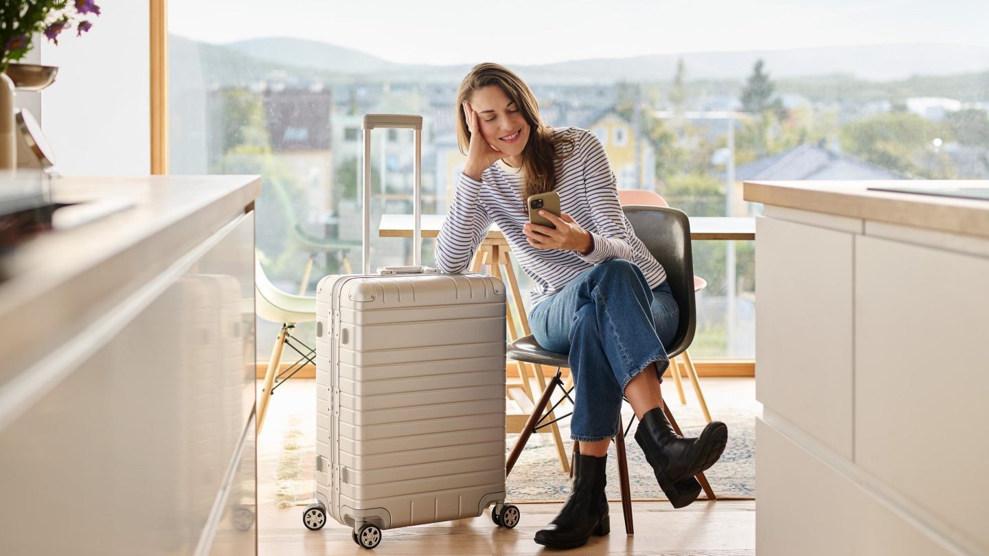 Woman sitting by a large suitcase, smiling at her phone.