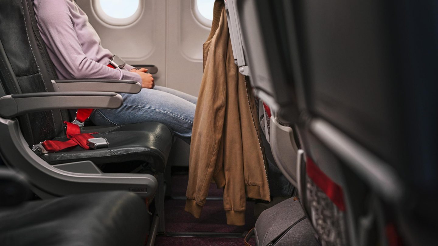 Passagier angeschnallt auf dem Flugzeugsitz. Jacke auf der Rückenlehne, Blick aus dem Fenster.