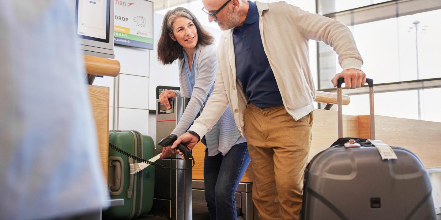 A smiling couple at an airport walking with their suitcases.