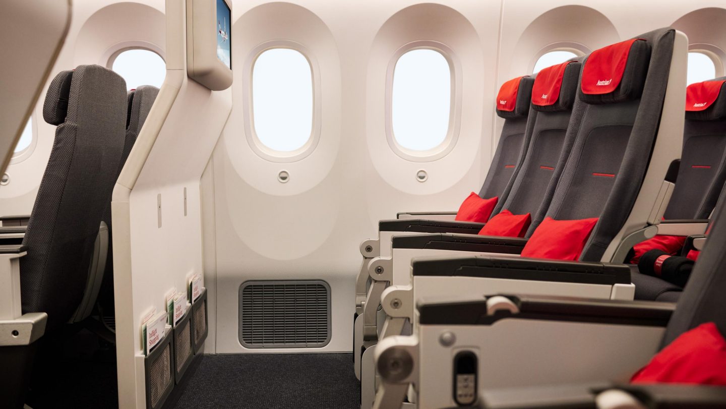 Airplane cabin interior with three empty black seats, red headrests, and oval windows.
