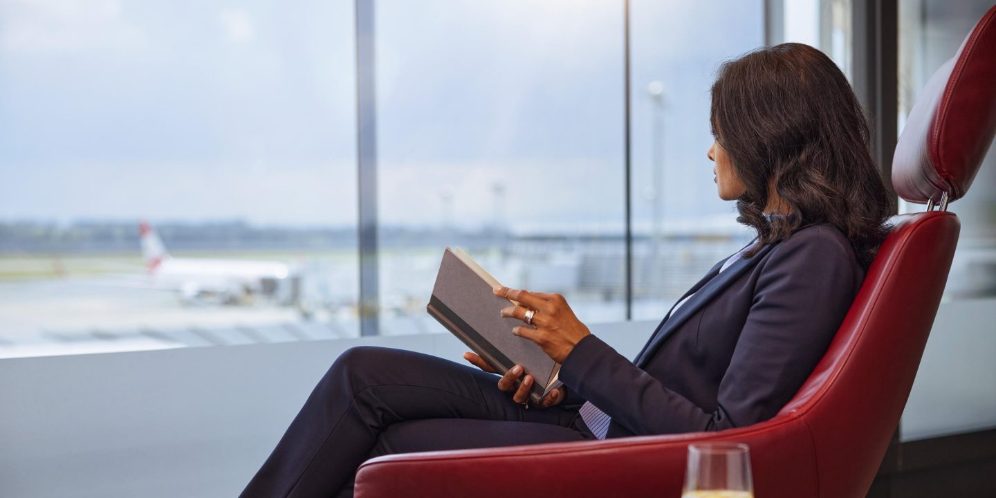 A business traveler reading a book in an airport lounge with a view of a plane.