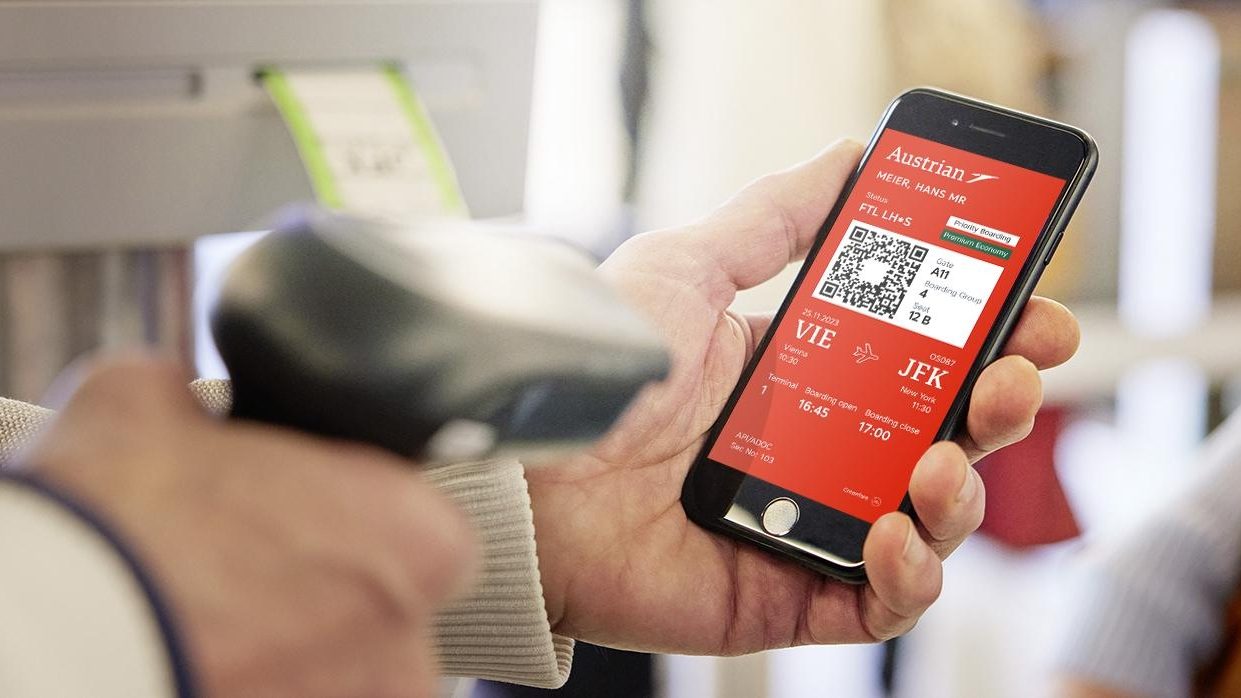 A person holding a smartphone displaying an Austrian Airlines boarding pass for a flight from Vienna (VIE) to New York (JFK).