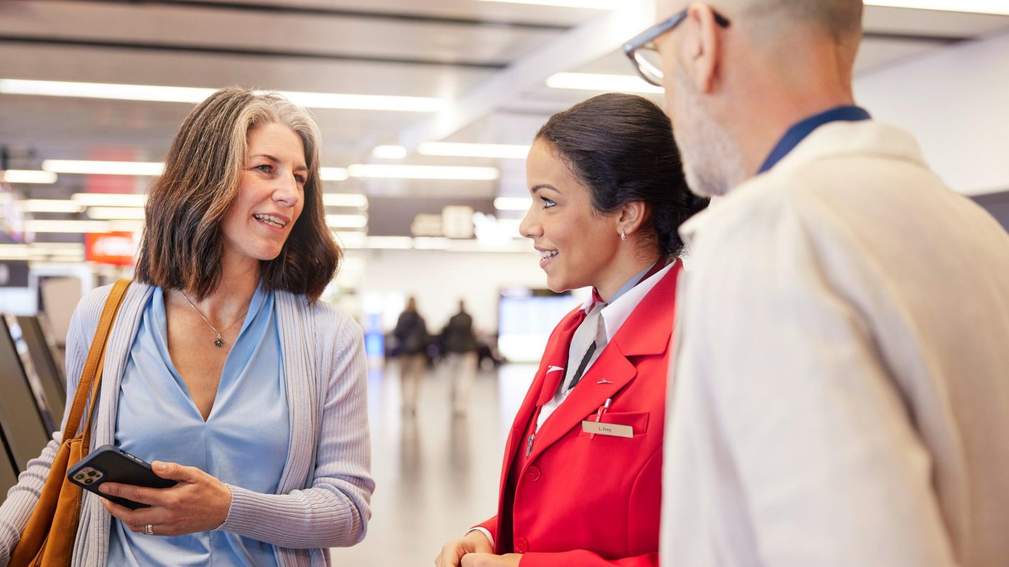 A female airline staff member in a red uniform assisting a passenger couple at the airport.