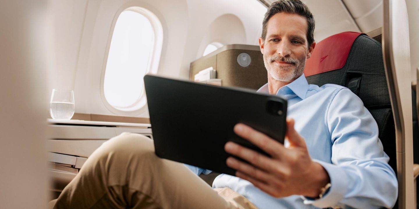 Ein Mann, der entspannt auf einem bequemen Business-Class-Sitz im Flugzeug ein Tablet benutzt.