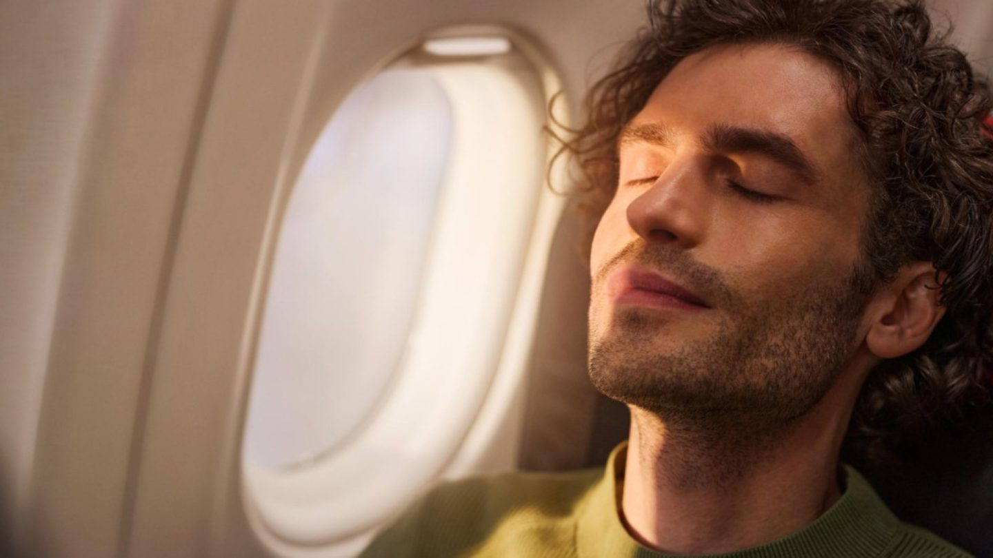 A passenger sleeps peacefully on a flight, their face illuminated by the sun.