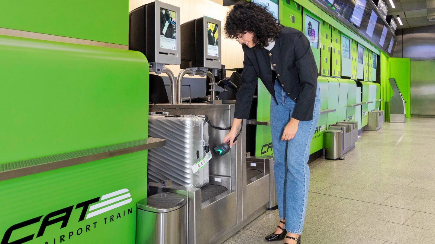 Person scanning luggage at self-check-in kiosk with CAT Airport branding.