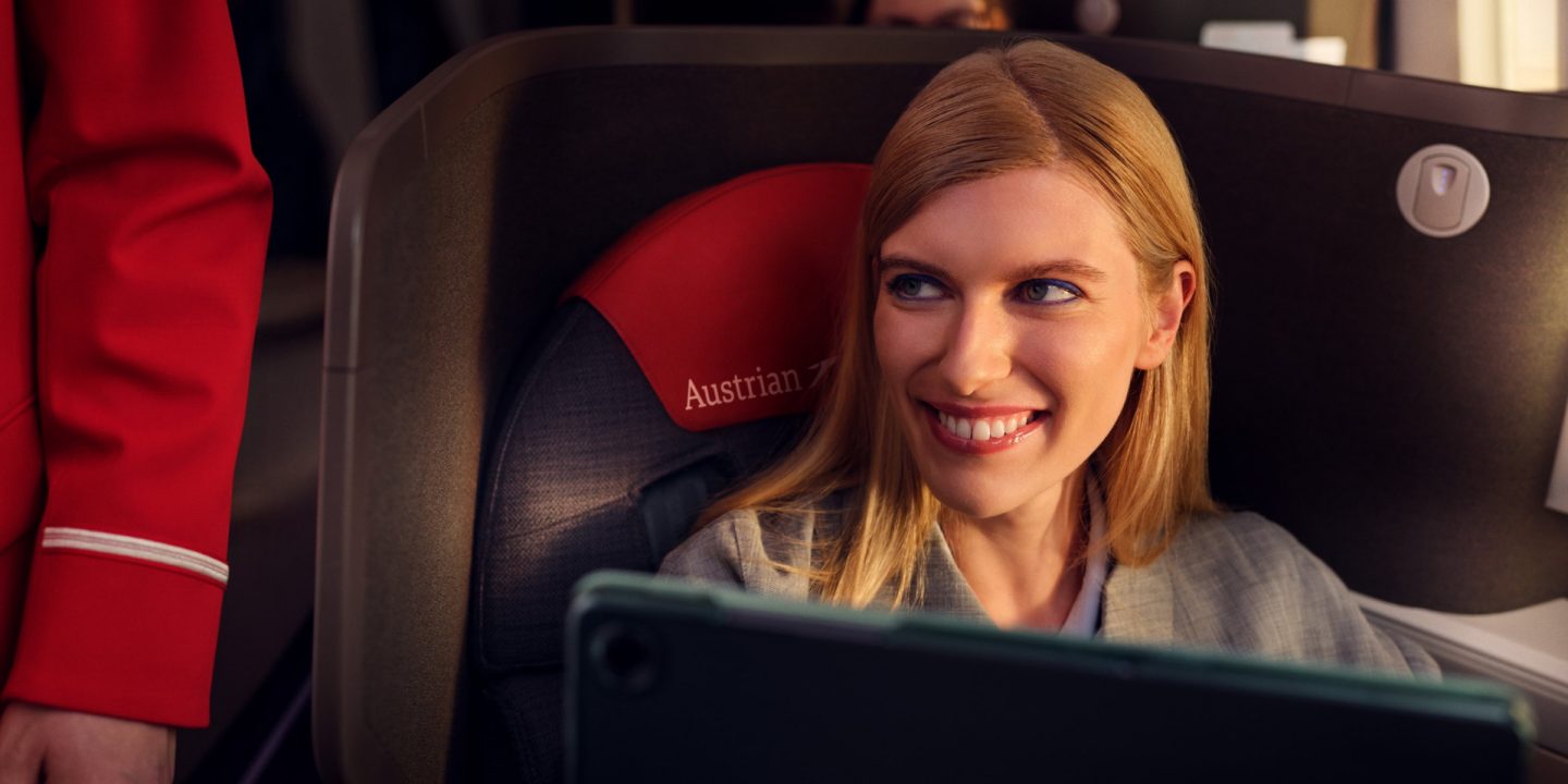 Ein lächelnder Passagier in der Business Class der Austrian Airlines blickt die Flugbegleiterin an.