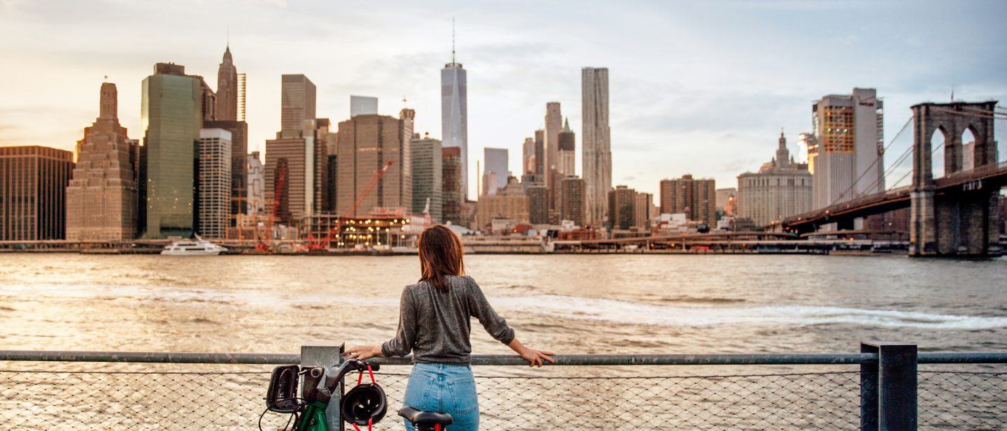 Frau mit Fahrrad vor New Yorker Skyline