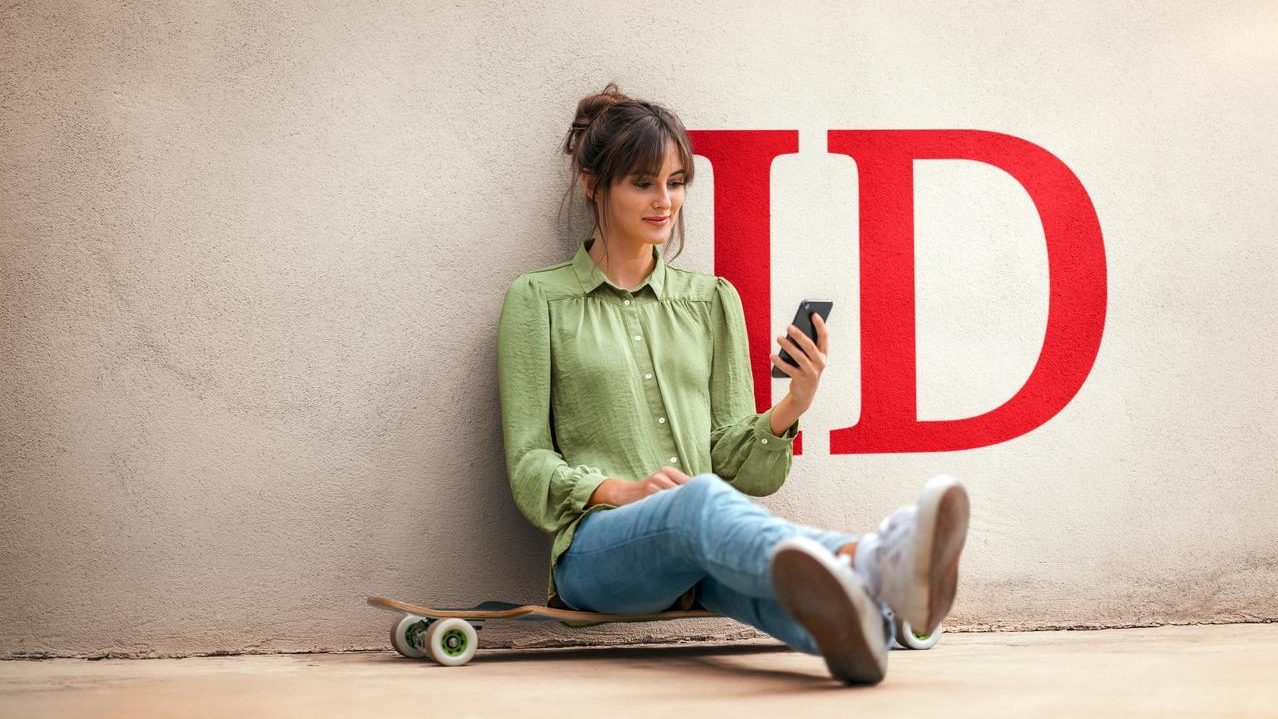Person sitting on a skateboard against a wall, looking at their smartphone.