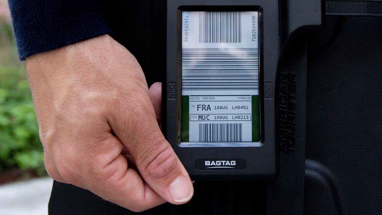 Hand adjusting a digital luggage tag on a black suitcase.