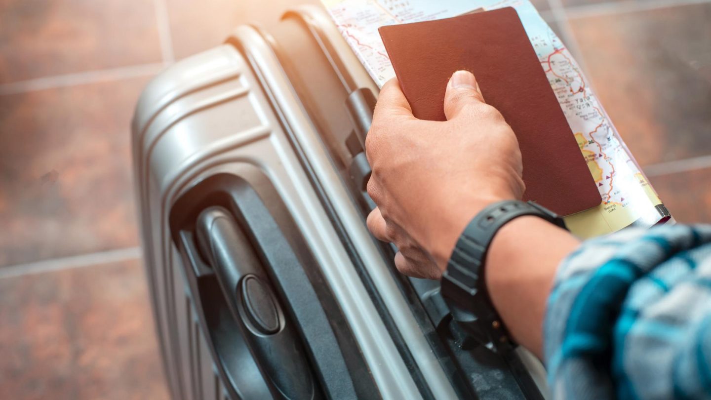 Hand holding a passport and map on a silver suitcase.