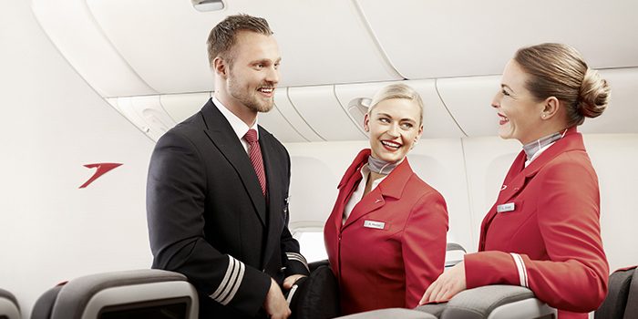 Three air stewardesses are engaged in conversation and smiling on an airplane, promoting a welcoming environment.
