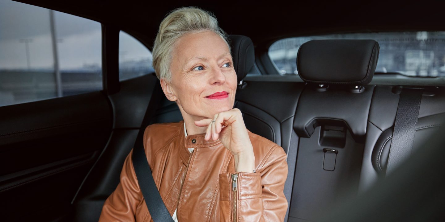 A woman in the back seat of a car looks thoughtfully out the window.