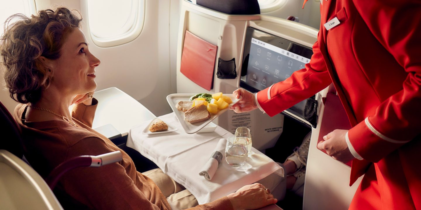 A woman enjoying a meal while seated in Business Class on an airplane.