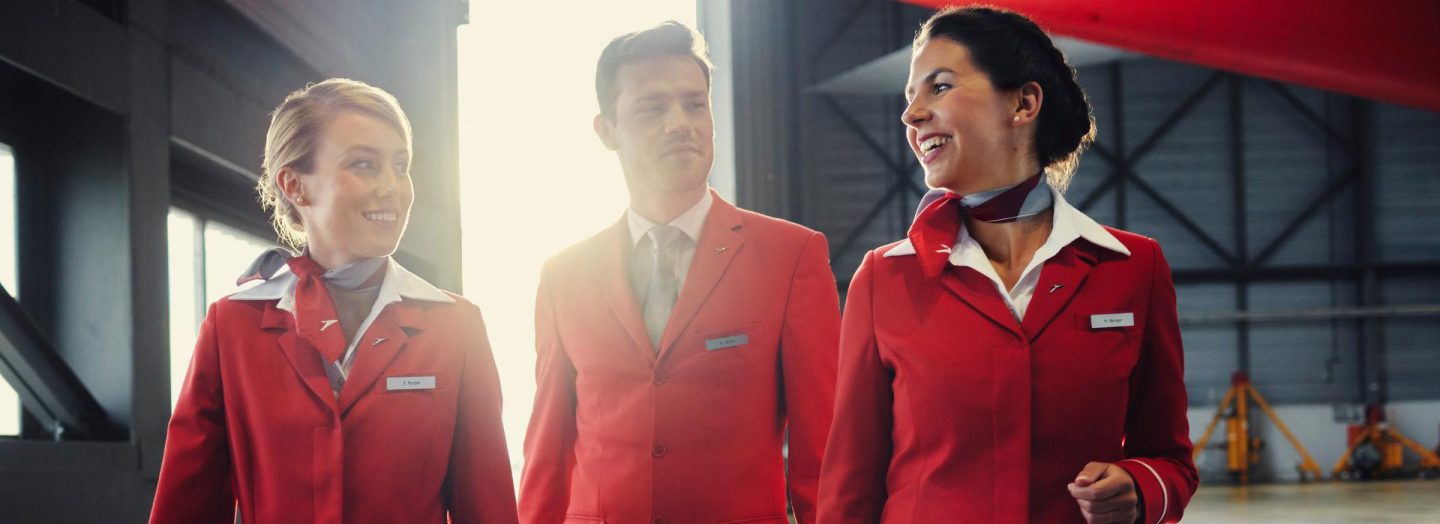 Three Austrian employees in red uniforms walk through an aircraft hangar together