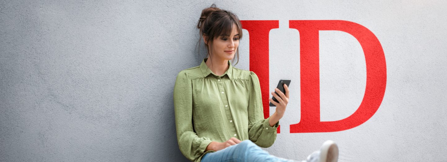 Young woman sitting on skateboard, using smartphone