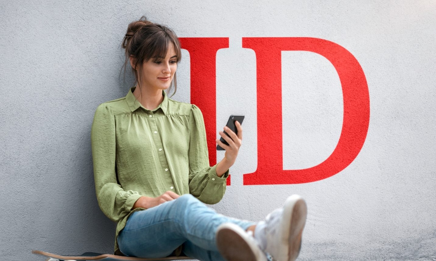 Young woman sitting on skateboard, using smartphone